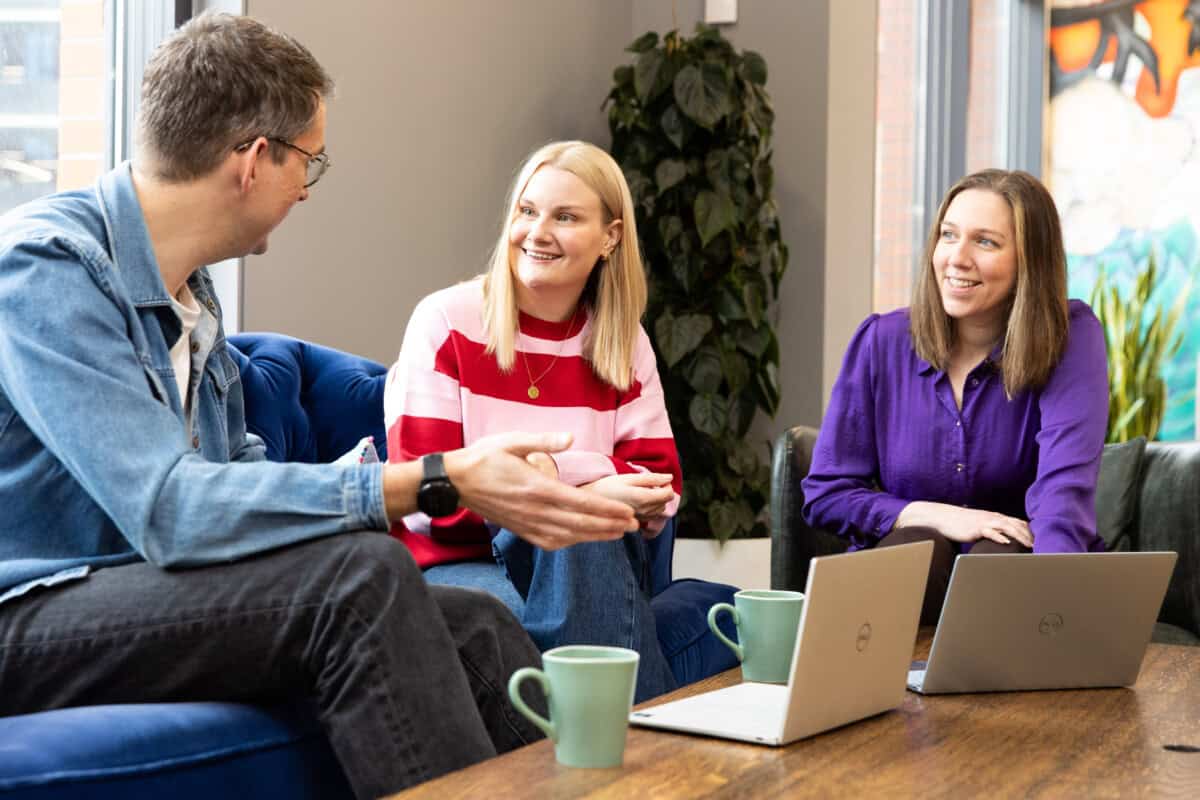 Three people sitting on a couch with laptops