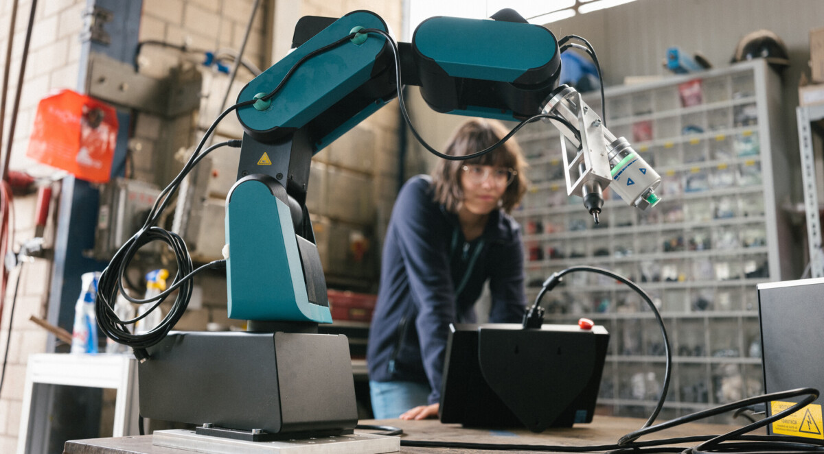 female technician programs a robot arm with a digital tablet